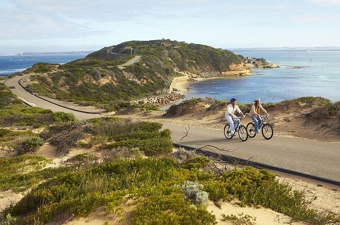 Two riders on the sealed road through the dunes above a bay at Point Nepean