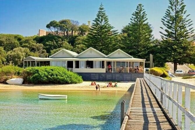 A timber jetty over clear water and beach houses under Norfolk pines on the bay