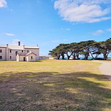 Old white buildings on a wide lawn under cypress trees at Point Nepean